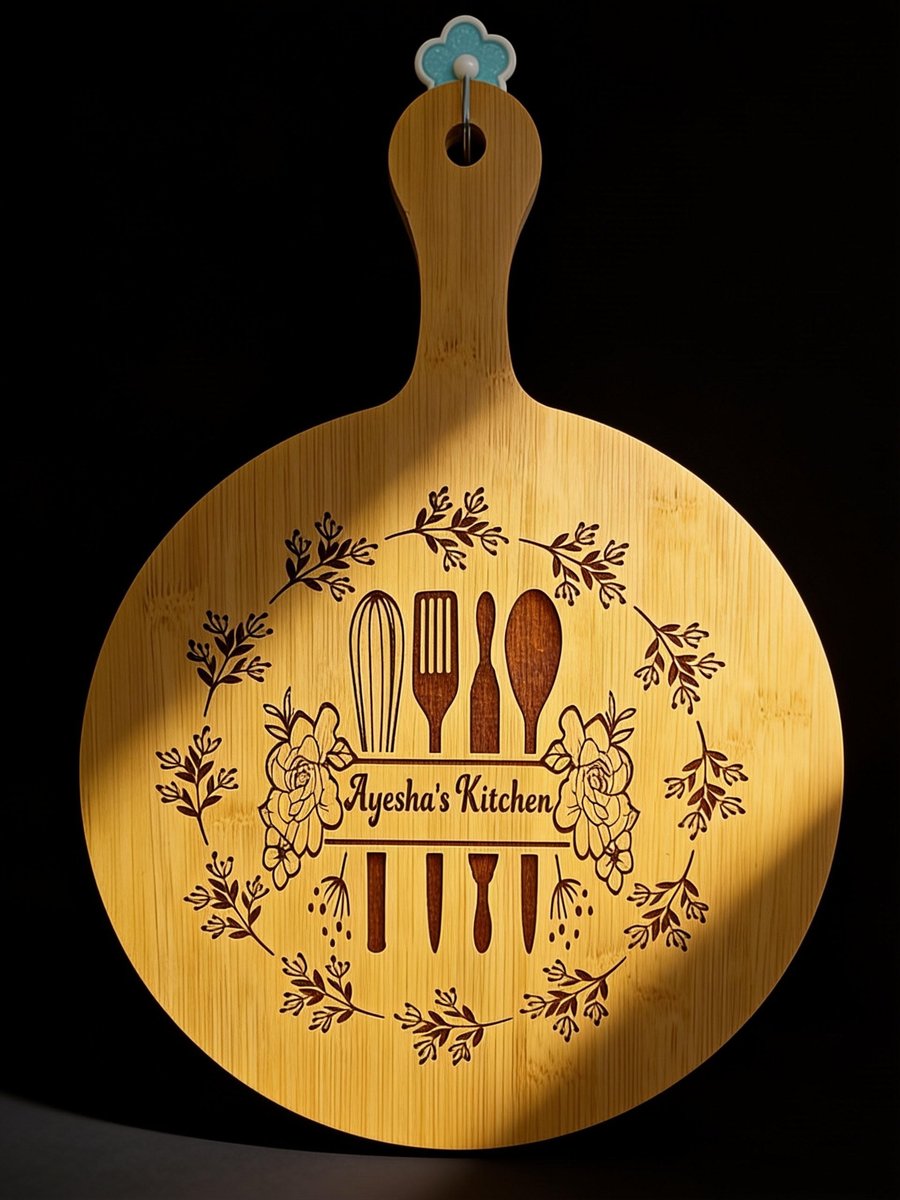 Round engraved wooden paddle board with kitchen utensils and floral wreath reading Ayesha's Kitchen